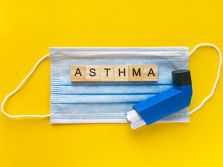 The word asthma made from wooden letters and inhaler on a blue medical face mask. Asthma treatment concept.