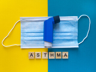 Top view of the blue inhaler on a medical face mask and the inscription Asthma made from wooden letters. Illness treatment concept.