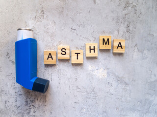 Top view of a blue inhaler and the inscription ASTHMA. The word is made of wooden letters.