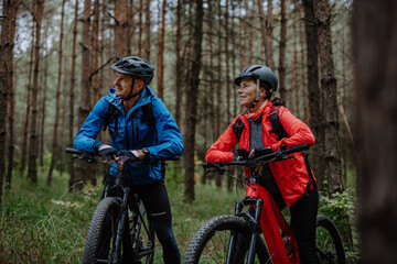 Senior couple bikers with e-bikes admiring nature outdoors in forest in autumn day.