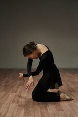 ballerina gracefully folds her arms in a dance, kneeling, on a gray background. dance aesthetics, grace, sensuality