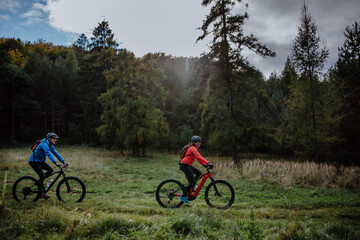 Fototapeta premium Side view of active senior couple riding bikes outdoors in forest in autumn day.