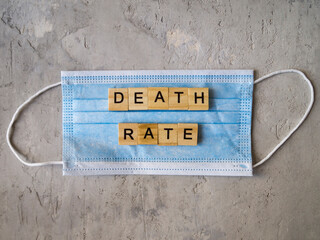 Words DEATH RATE lined with wooden letters on a background of blue surgical mask.