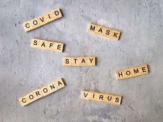 Words COVID CORONA VIRUS STAY HOME SAFE MASK laid out from wooden cube letters on a gray concrete background. Medical concept.