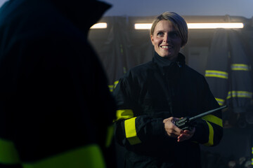 Happy mid adult female firefighter with walkie talkie in fire station at night.