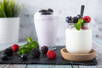 Yogurt decorated with blackberries, raspberries and blueberries. Smoothi with blackberries. Drinks in a minimalist rustic environment with plant out of focus in the background. Healthy and multivitami