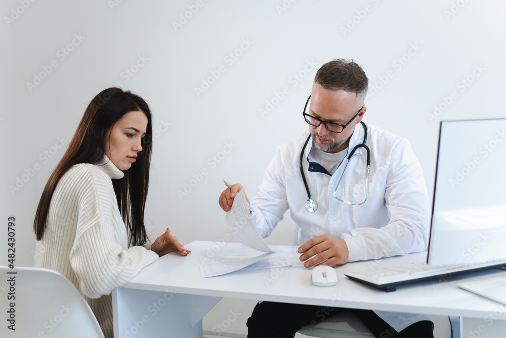 Wall mural Male doctor fills out medical documentation during the female patient's appointment