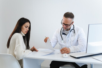 Male doctor fills out medical documentation during the female patient's appointment