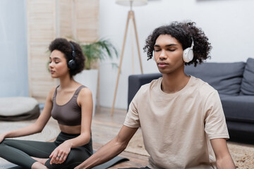 African american man in headphones meditating near girlfriend at home.