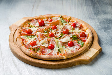 Pizza with Parma ham, greens and parmesan on wooden board on grey table