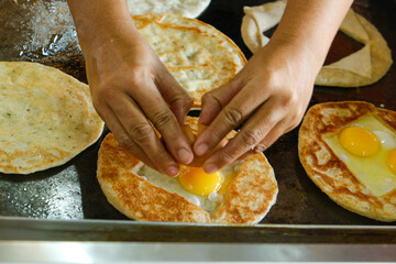 Selective focus with noise effrct added of paratha and motion blur hand try to break the egg. Making 
