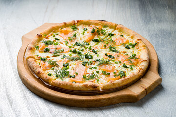 Pizza with salmon, cheese and green onion on the board on grey table