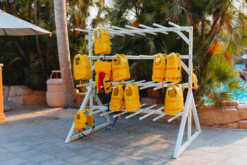 Stack of hanging yellow life vests on hangers outside during the marine activities, safety clothing, protection concept