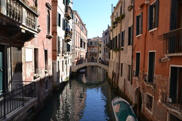 canals of venice, italy, with old buildings on the side, in a gondola ride, in red tones, in the blue sky, reflection in the water