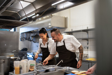 Happy chef and cook working on their dishes indoors in restaurant kitchen. - obrazy, fototapety, plakaty