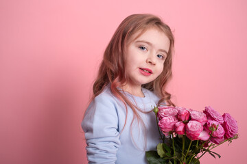 portrait of cute little girl in blue dress holding bouquet of pink roses on pink background
