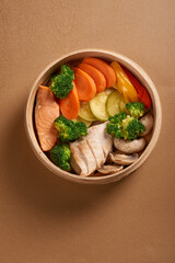 Bowl with salmon and chicken on brown background