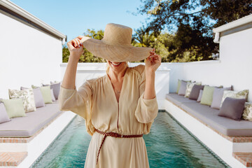 Glamorous tourist woman tipping her summer hat outdoors