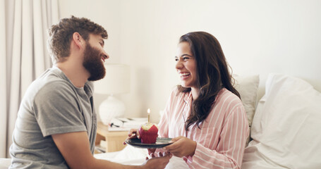 happy birthday to my beautiful wife. Shot of a young man surprising his wife with a cupcake in bed at home.