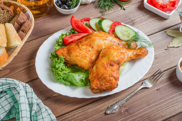 Fried crispy chicken legs with fresh vegetables and herbs on a white plate on a dark wooden background