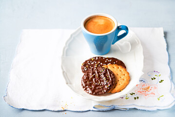 Chocolate cookies with colorful sprinkles and coffee for brunch or breakfast on light blue background.