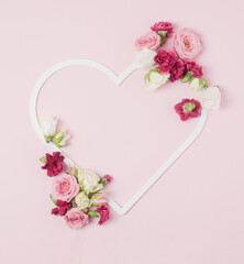 Heart shaped frame with colorful spring flowers spilled around it on a pastel pink background. Valentine's day romantic backdrop