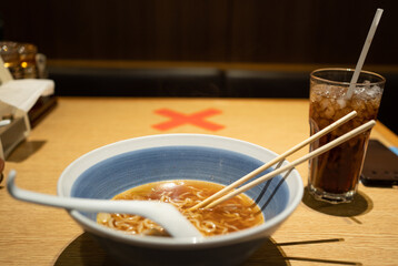 Selective focus of a bowl with remaining ramen and cold drink in glass placed on table with red...