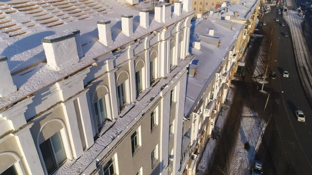 Multistory classic style building with snowy cornices and arch windows on city street at sunset in winter bird eye view