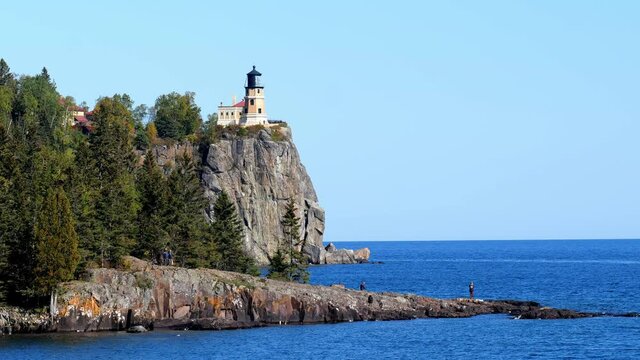 Split Rock Light House on the north shore of Lake Superior in Minnesota, and a few visitors on an outcrop into the beautiful blue water. A popular travel destination for tourists on the great lake.