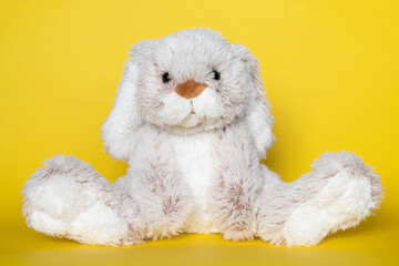 Stuffed soft toy bunny on yellow background. Easter concept. Beautiful white toy bunny sitting on...