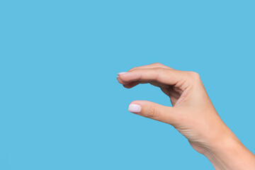Closeup view stock photography  of beautiful white manicured female hand showing small size of virtual invisible object with help of fingers isolated on blue background