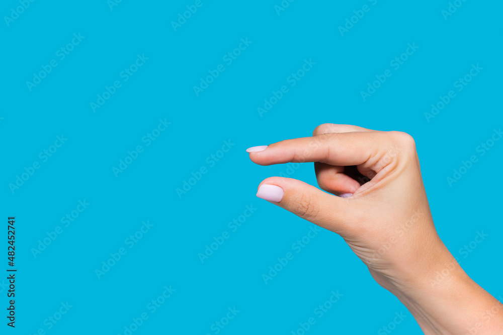 Wall mural Closeup view stock photography  of beautiful white manicured female hand showing small size of virtual invisible object with help of two fingers isolated on blue background