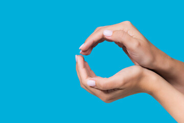 Closeup view photography  of two beautiful white manicured female hands holding virtual invisible object of round shape isolated on blue background. Gesture of holding, care, protection of object