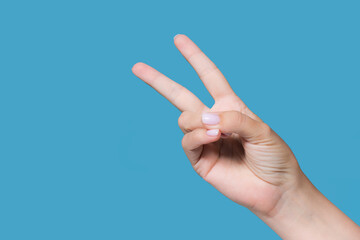 Closeup view stock photography of one beautiful manicured female hand isolated on blue background. Woman showing raised two fingers up gesture counting down or showing V (victory) non verbal sign