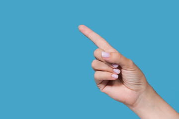 Closeup view stock photography of one beautiful manicured female hand isolated on blue background. Woman showing raised one index (pointer) finger up gesture