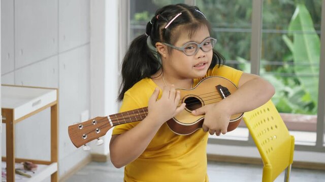 The cute little girl with down syndrome plays the ukulele in sensory activity, development exercises at home. Education and special child concept