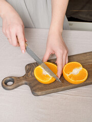 Young woman's hands with a knife cut an orange for making fresh juice at the kitchen. Healthy or dietary food concept. Close up. Cropped view. Bright yellow orange on cutting board. Copy space