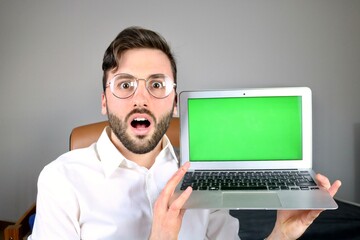 Young surprised Computer scientist showing laptop with green screen display 