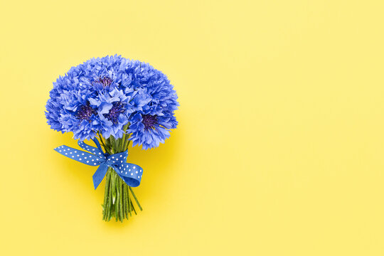 Blue cornflower bouquet decorated with ribbon on a yellow background. Greeting card