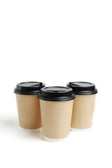 Three eco friendly paper craft cups for coffee with black lid on the white background. Zero waste, plastic free concept. Sustainable lifestyle. Composition with front view.