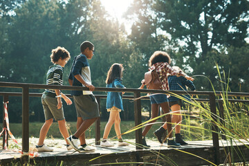 Adventure, here we come. Shot of a group of teenagers walking across a bridge in nature at summer camp. - Powered by Adobe