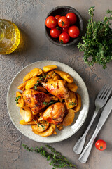 Baked chicken legs and potatoes with oranges, garlic and onions in a plate on a dark culinary background. Top view
