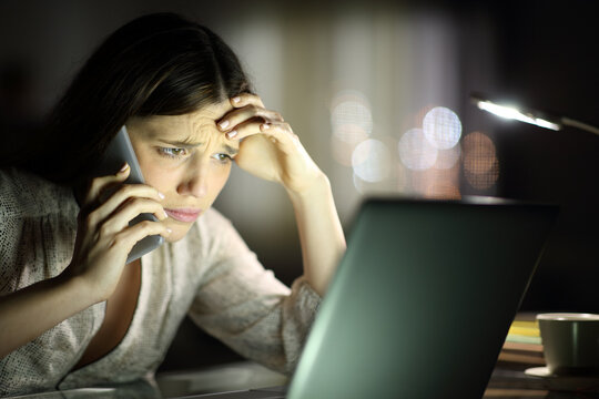 Worried woman checking laptop and calling on phone in the night