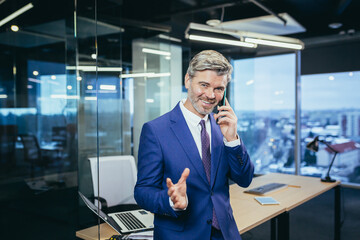 Successful boss working in a modern office, gray-haired businessman talking on the phone