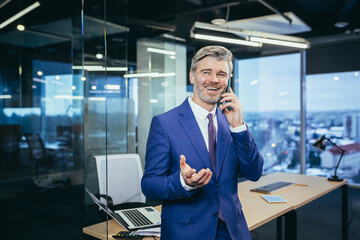 Successful boss working in a modern office, gray-haired businessman talking on the phone