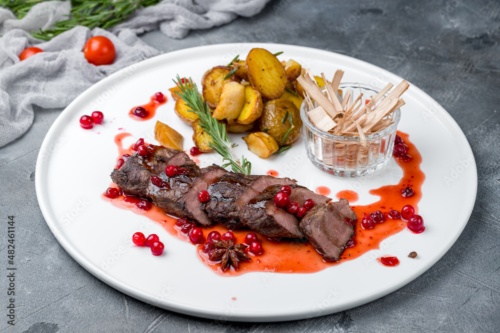 Sticker Beef steak sliced with mini potatoes and berry sauce on white plate on grey table