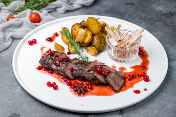 Beef steak sliced with mini potatoes and berry sauce on white plate on grey table