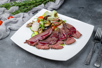 salad with sliced dry-cured venison and vegetables on grey table