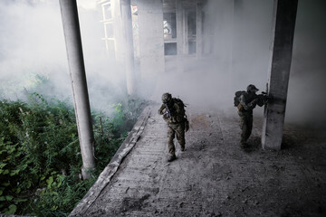 Two soldiers in camouflage uniforms with rifles scout the building