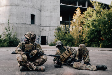Two military men are resting while sitting on the ground